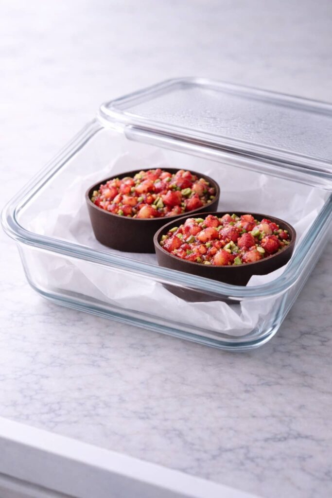 Dubai chocolate strawberry cups stored in a glass container lined with parchment paper
