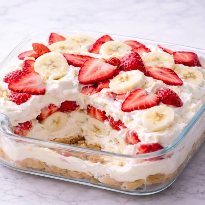 Layered strawberry cheesecake banana pudding dessert in glass baking dish