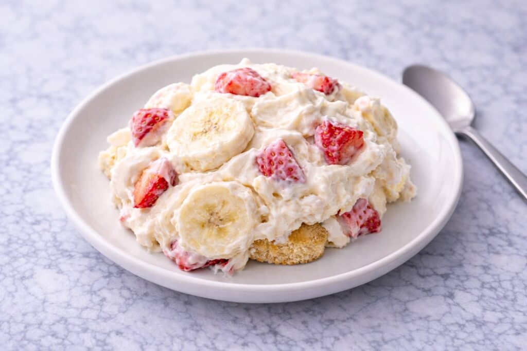 Serving of strawberry cheesecake banana pudding on white plate showing creamy layers and fruit