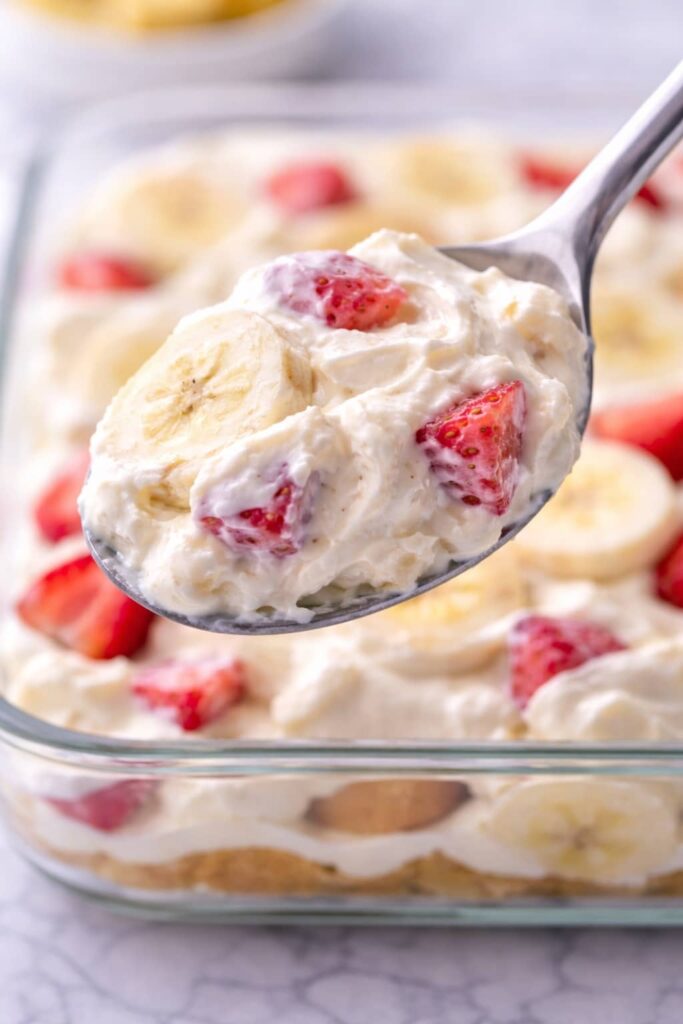 Close up spoonful of strawberry cheesecake banana pudding showing creamy texture and fruit pieces