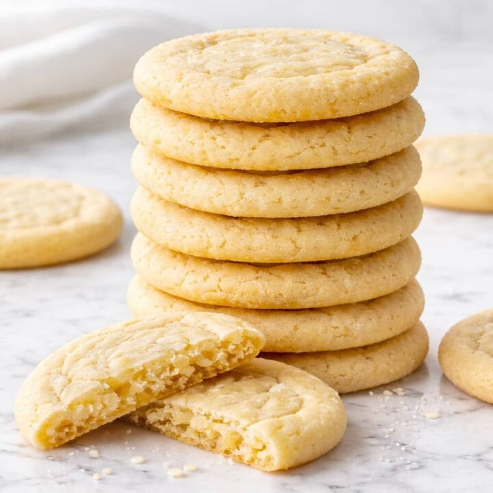Soft and chewy sugar cookies stacked on white marble surface with one cookie broken open showing tender center