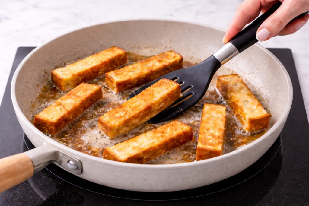 Cooking French toast sticks in butter in a skillet on an induction cooktop