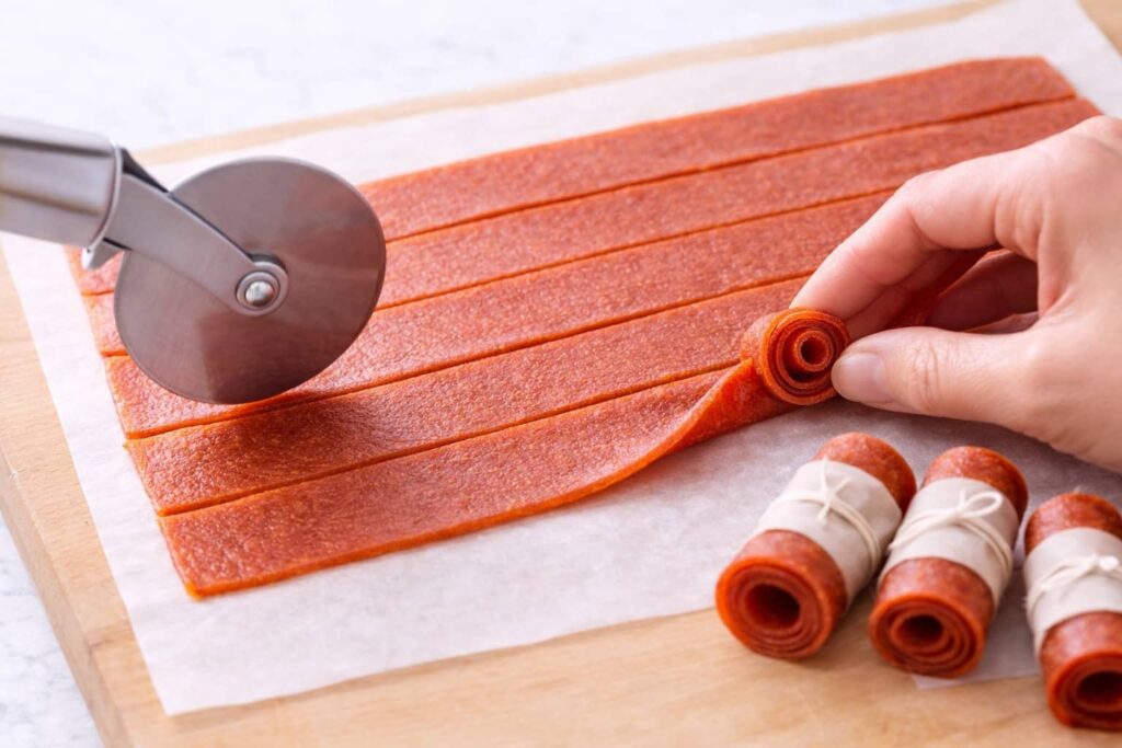 How to Cut and Roll Fruit Roll Ups cutting and rolling homemade fruit roll ups into strips using a pizza cutter