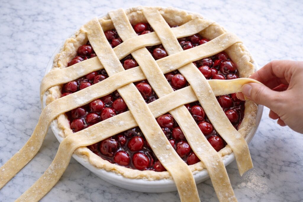 Assembling lattice crust on cherry pie with pastry strips over cherry filling