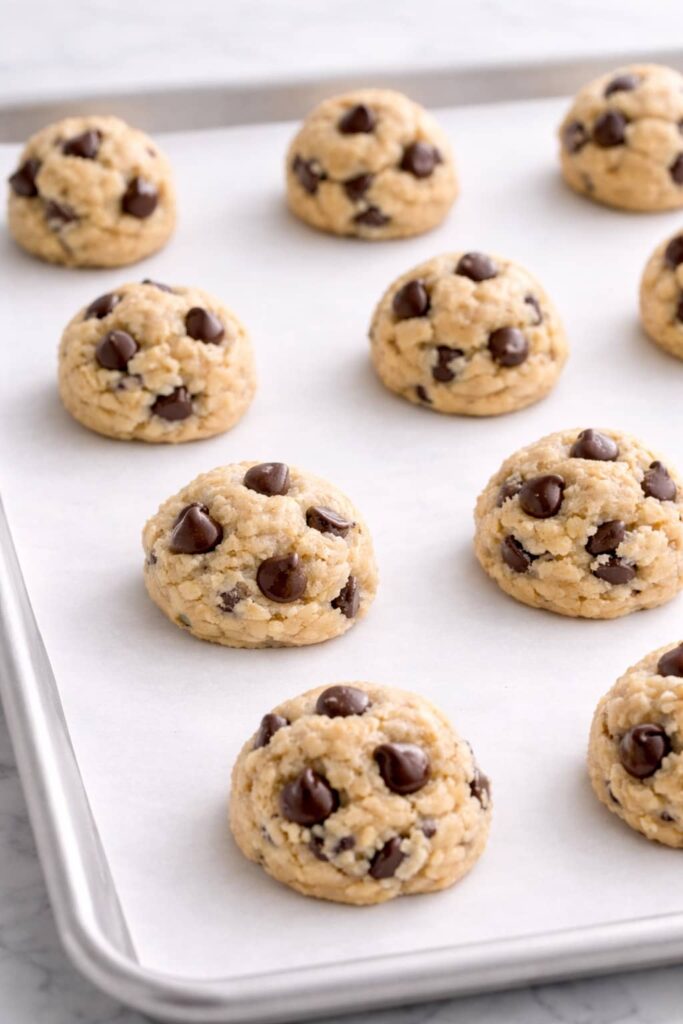 Chocolate chip cookie dough balls on parchment lined baking sheet before baking