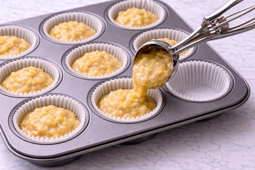 scooping banana muffin batter into muffin pan
