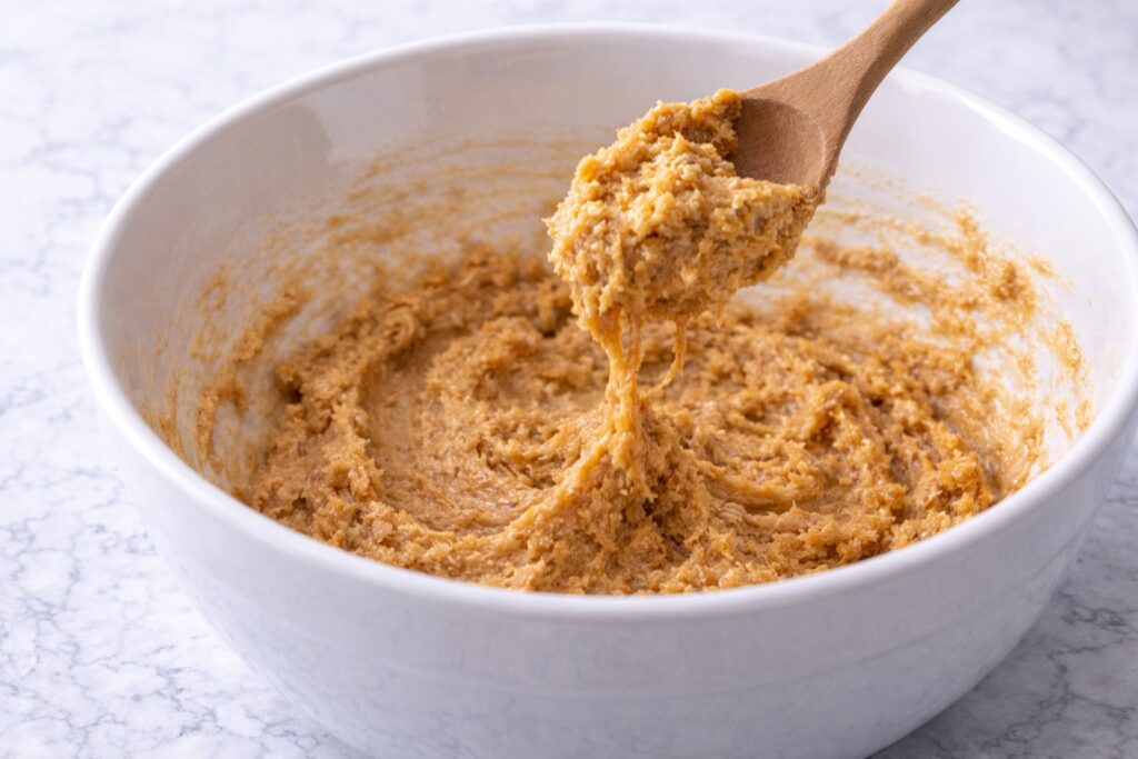 mixing peanut butter cookie dough in white bowl with wooden spoon