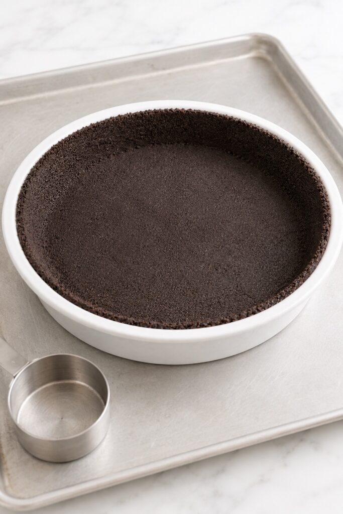 Oreo cookie crust pressed evenly across the bottom and sides of a white pie dish before baking.