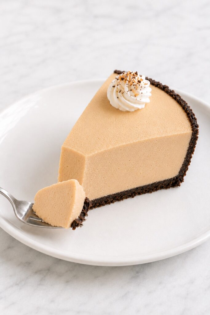 Fork lifting a creamy bite from a plated slice of Peanut Butter Pie with Oreo crust.