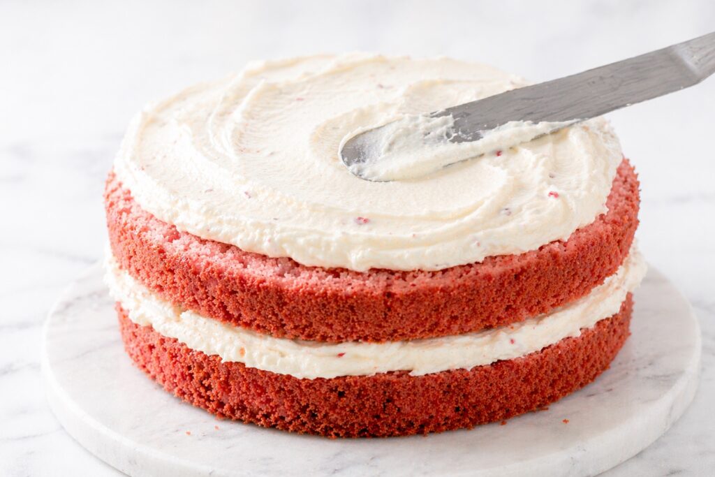 Layering Strawberry Cake with Frosting spreading cream cheese frosting between strawberry cake layers soft texture