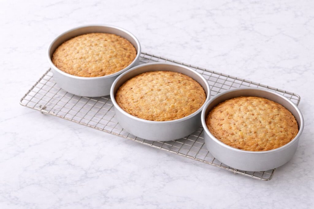 Baked Hummingbird Cake Layers Freshly baked hummingbird cake layers cooling in pans on a rack with golden tops