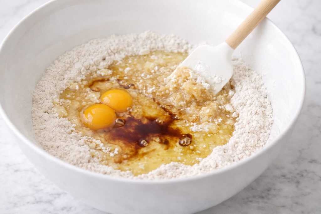 Adding Wet Ingredients to Hummingbird Cake Batter Wet ingredients added to dry mixture for hummingbird cake including eggs oil and vanilla