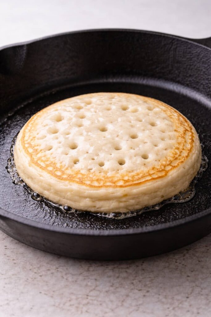 Sourdough discard pancake cooking in skillet with bubbles forming on surface