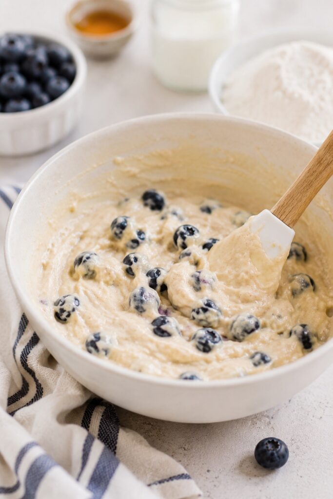 folding fresh blueberries into whole wheat healthy blueberry muffin batter in white mixing bowl
