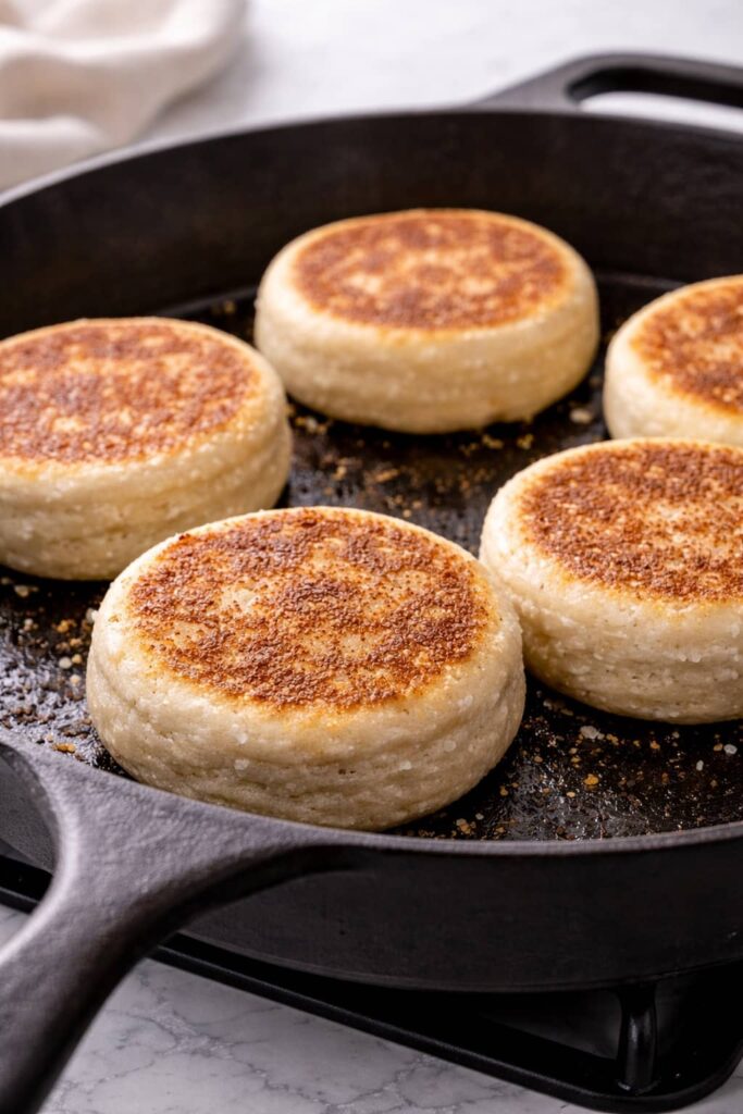Sourdough English muffins cooking in a cast iron skillet until golden brown