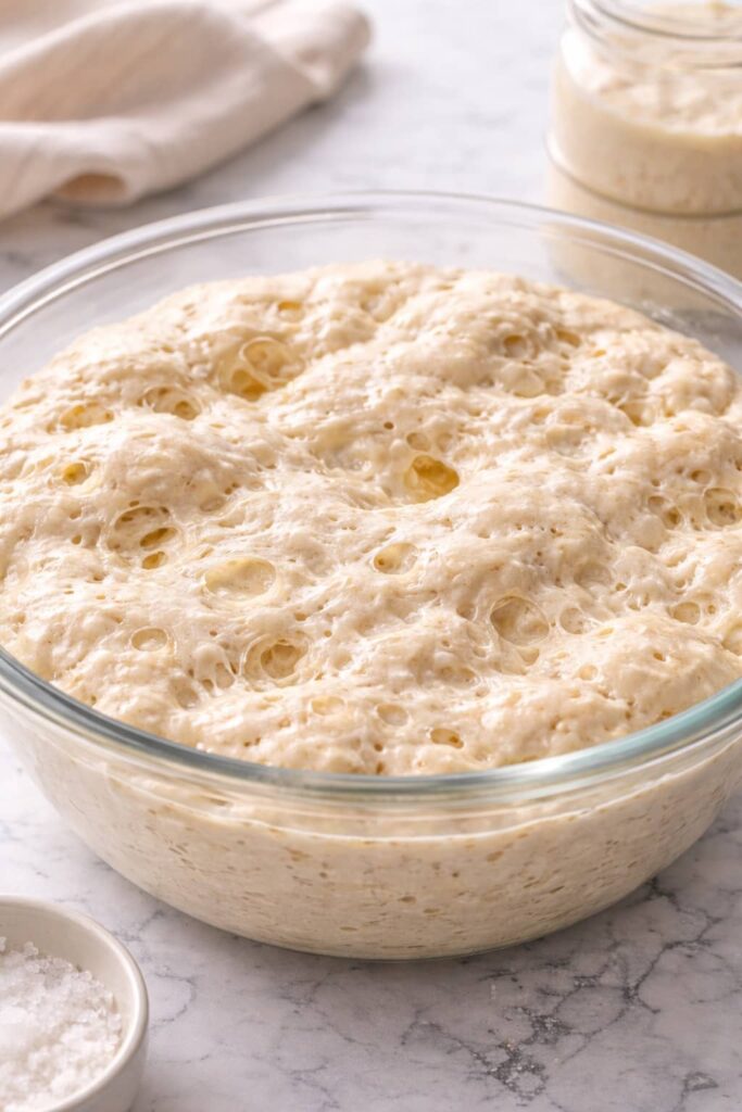 Naturally fermented sourdough English muffin dough showing active bubbles and airy structure in a glass bowl