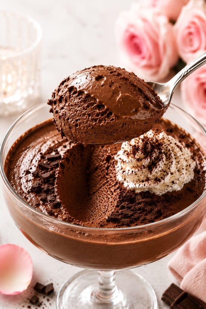 Extra Dark Chocolate Mousse for Valentine’s Day Extra dark chocolate mousse served in an elegant dessert glass with a silky glossy texture and a creamy spoon scoop lifted from the center. Romantic Valentine’s Day dessert styling with soft natural light, chocolate shavings, whipped cream, and a luxurious homemade dessert atmosphere.