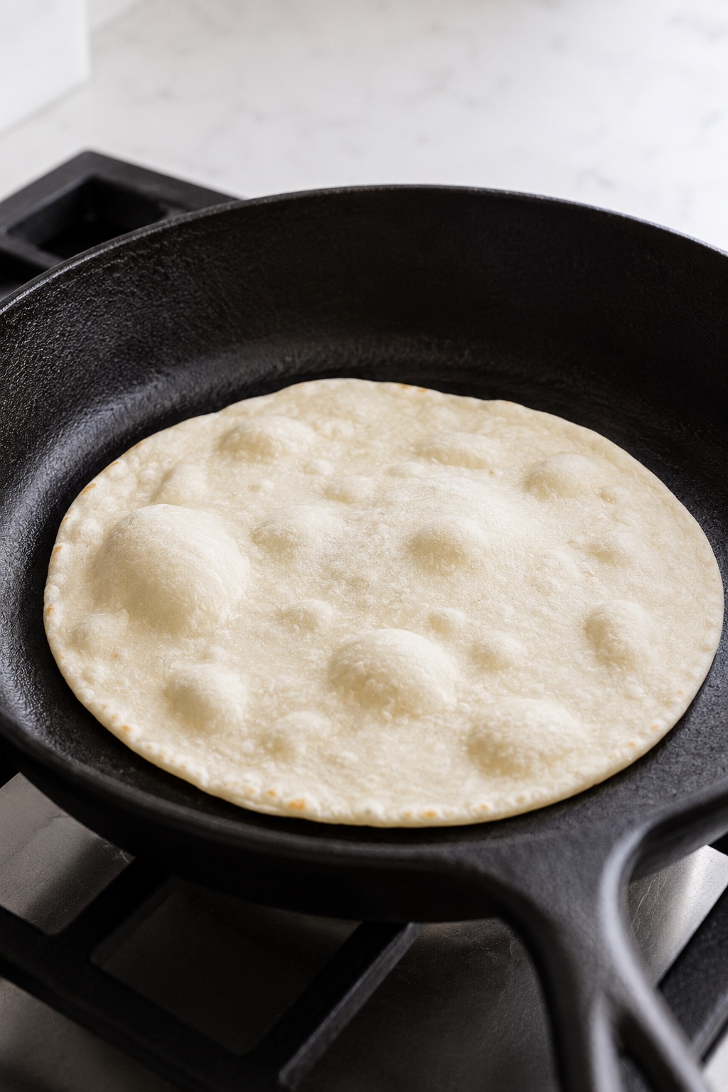 A sourdough discard tortilla forming small air bubbles as its first side cooks in a dry cast-iron skillet.