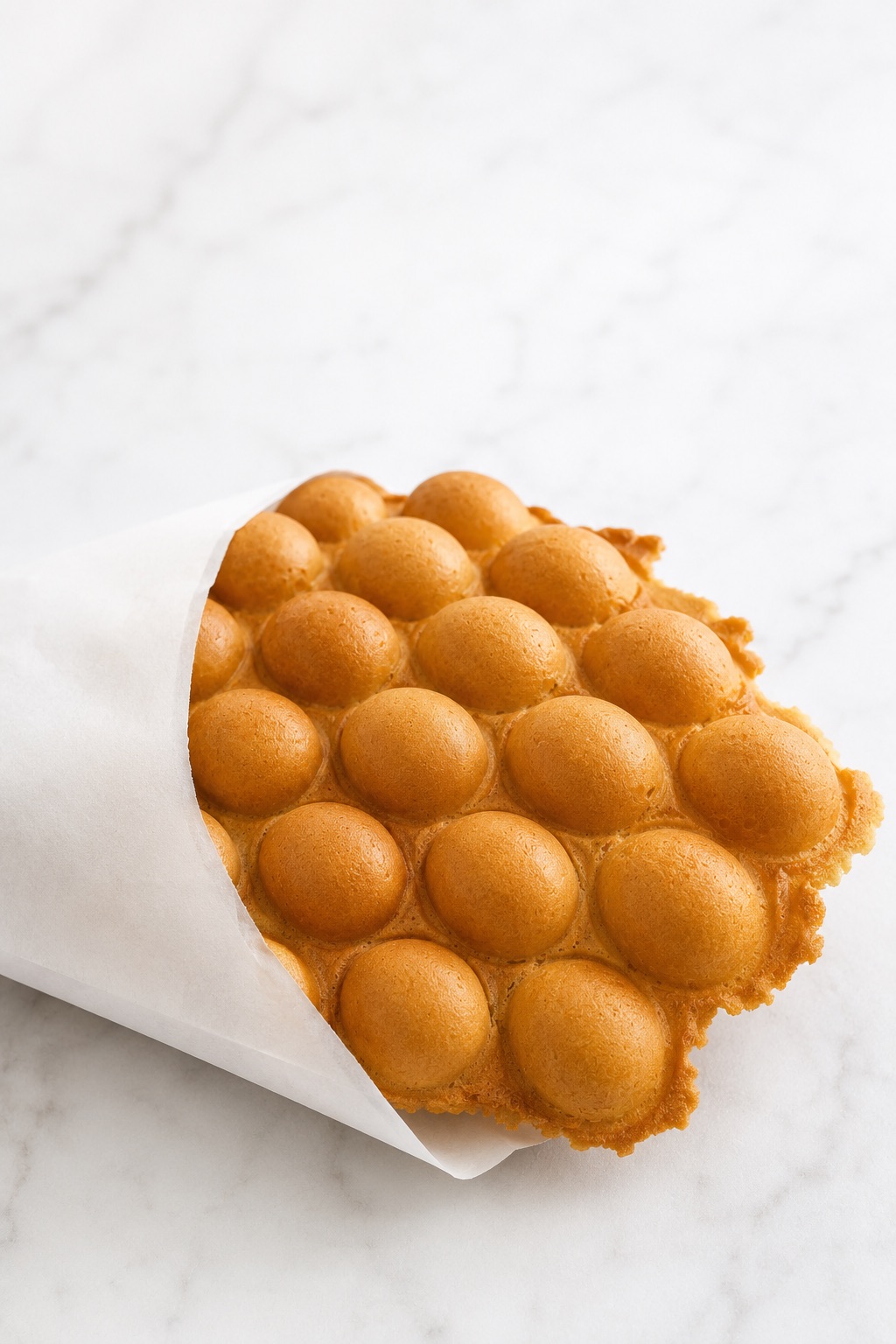 Warm plain Hong Kong Bubble Waffle served in a simple white paper sleeve.