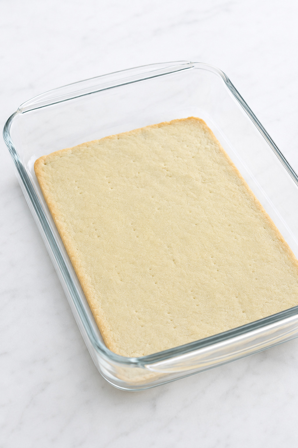 Matte, lightly set par-baked crescent dough in a clear glass baking dish.