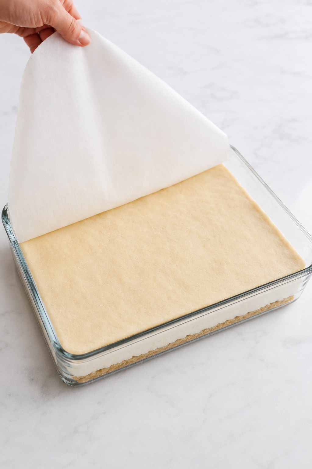 A cold crescent dough sheet transferred from parchment over the cheesecake filling.