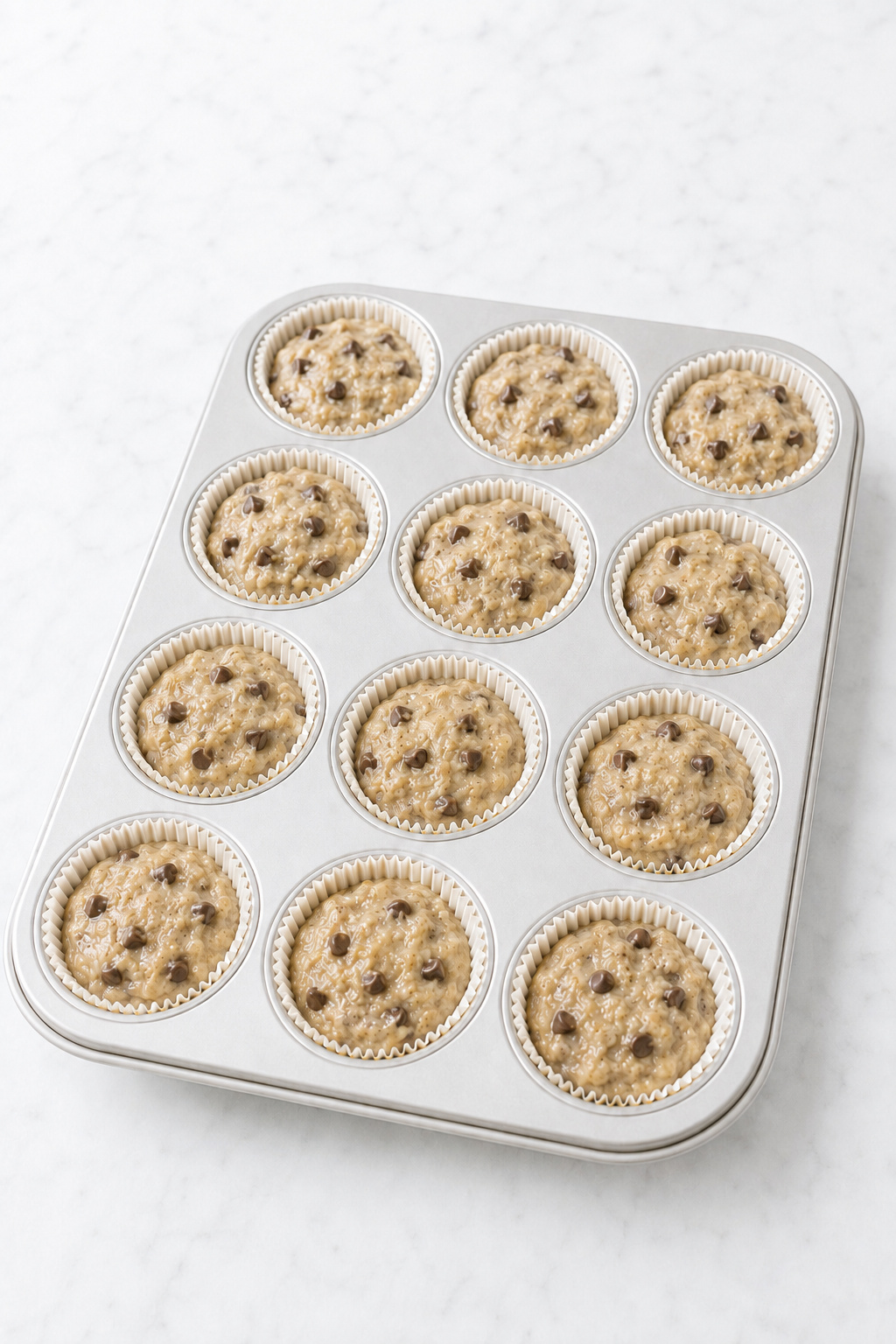 Banana chocolate chip muffin batter divided evenly among 12 lined muffin cups.