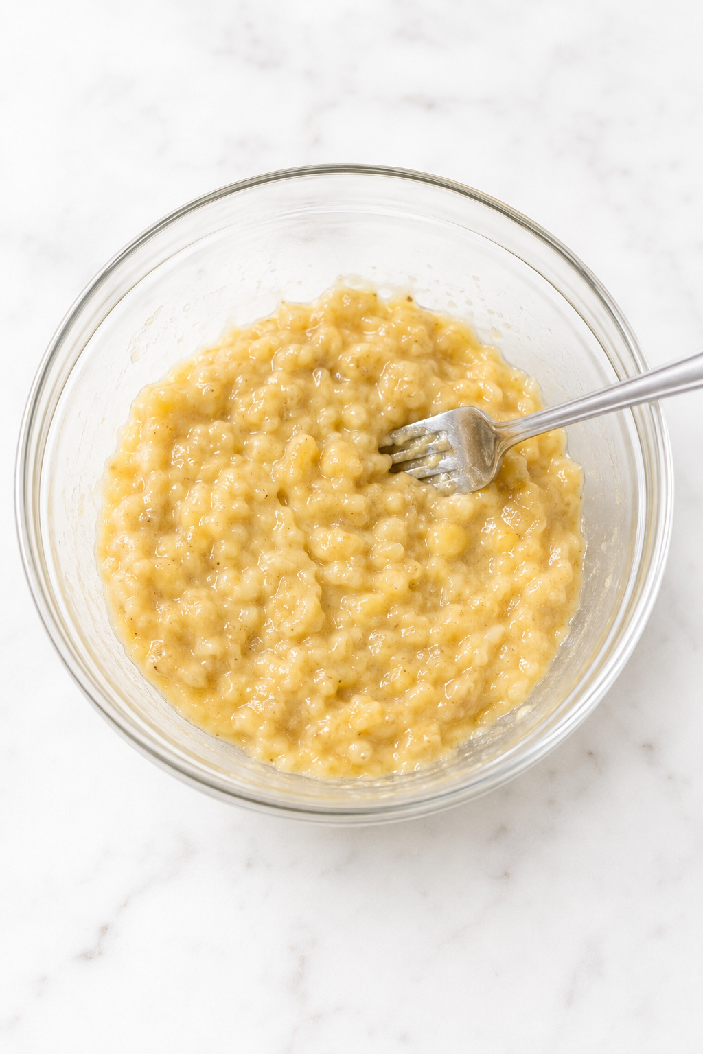 Thick glossy mashed banana with a few small pieces for banana muffin batter.