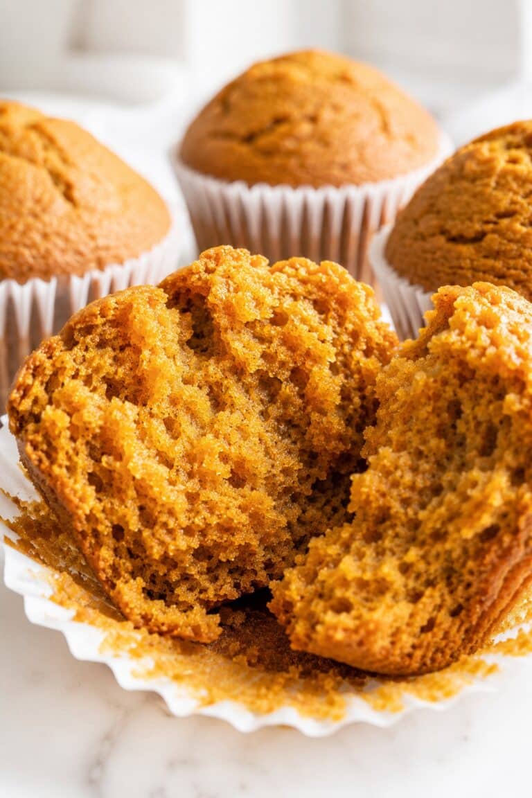 Pumpkin muffin broken open to show a moist orange crumb, with whole muffins behind it