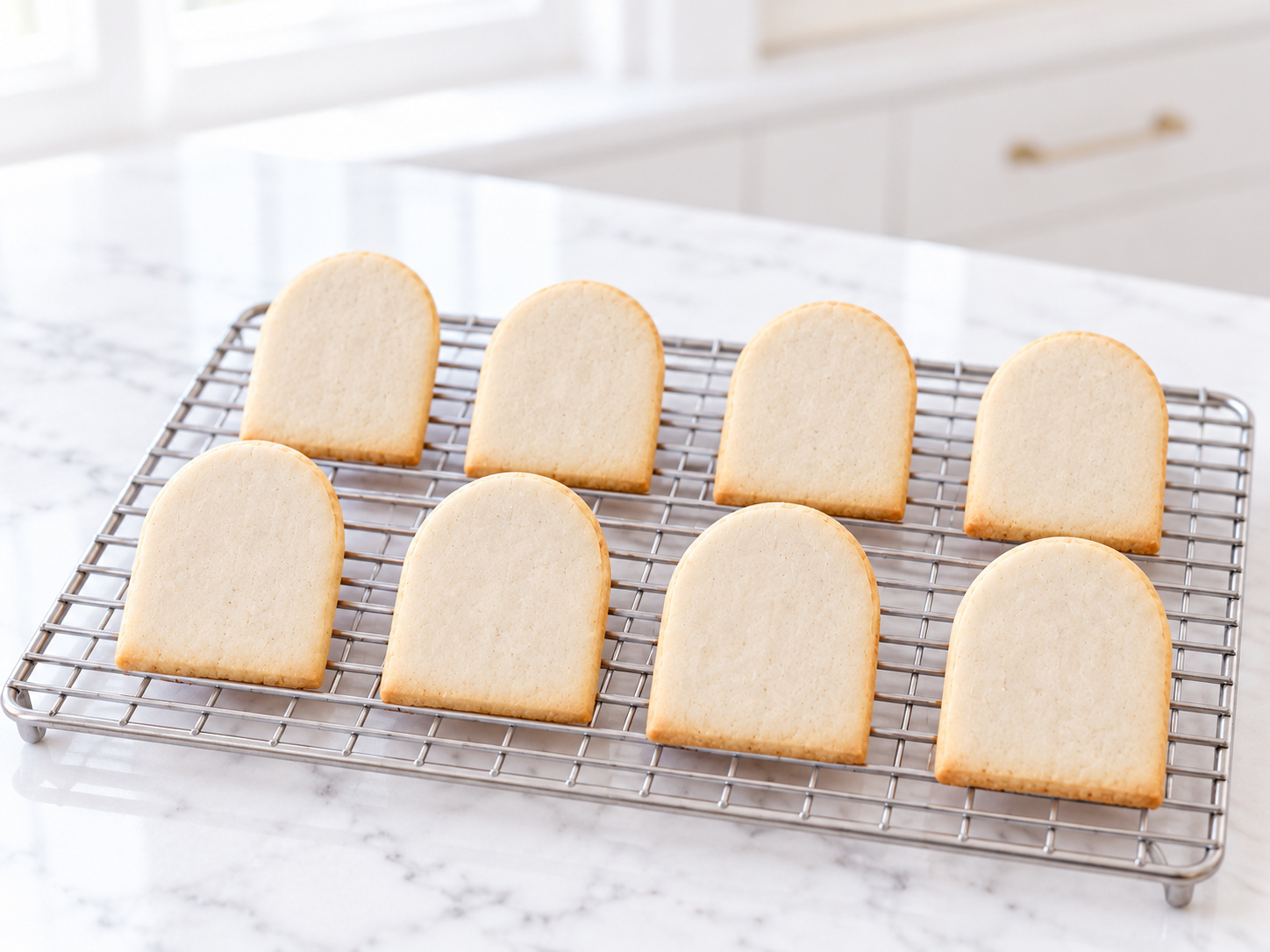 Eight pale baked shortbread tombstones with lightly golden edges cooling on a wire rack