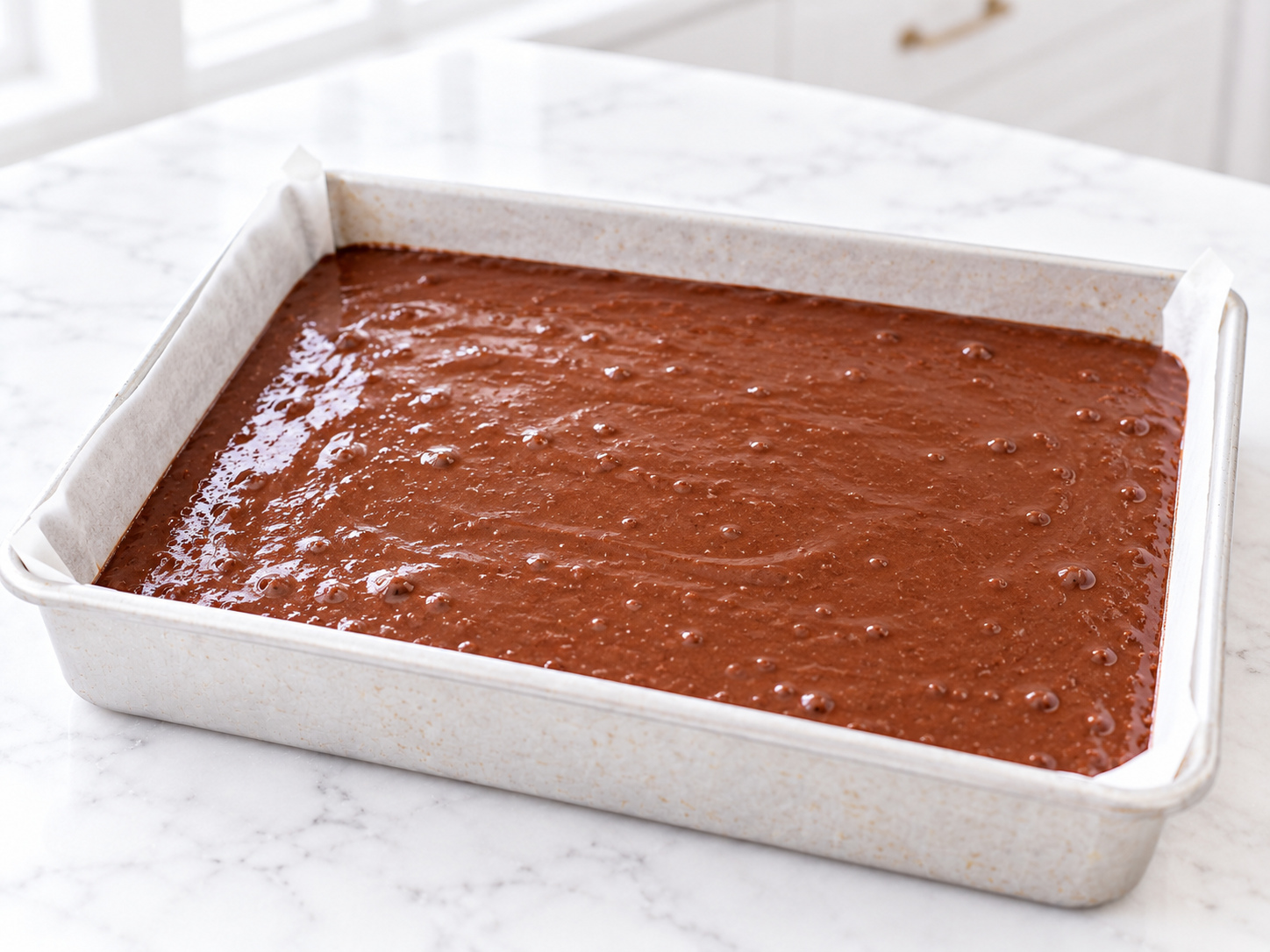 Chocolate cake batter spread evenly in a rectangular metal baking pan